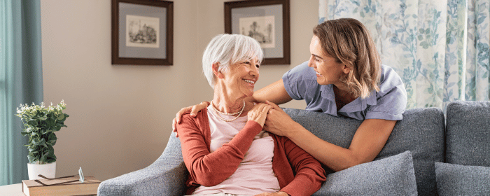 Senior woman smiling as she sits on a couch, comforted by a younger woman beside her, symbolizing the care and reassurance provided by New Jersey medical alert systems.