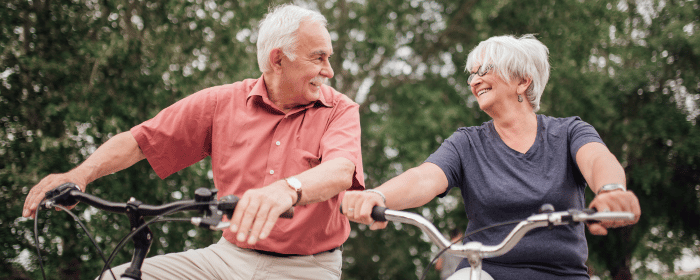 Senior couple biking outdoors, smiling at each other, symbolizing active and independent living. Explore reliable Medical Alert Systems in Michigan.